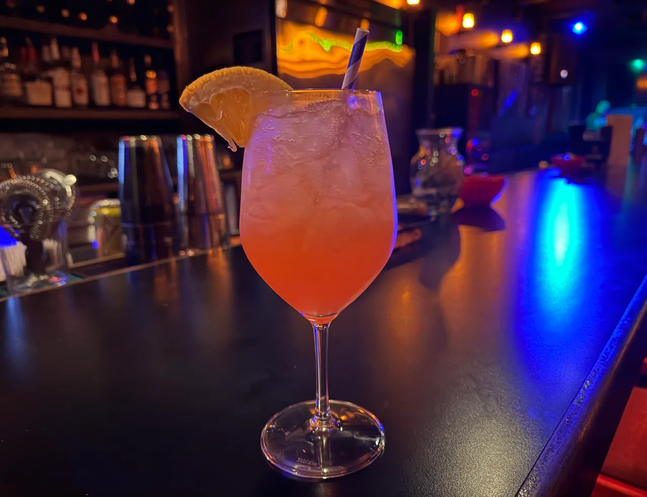 Spritz alaranjado em taça de vinho com gelo e fatia de laranja, sobre o balcão de um bar