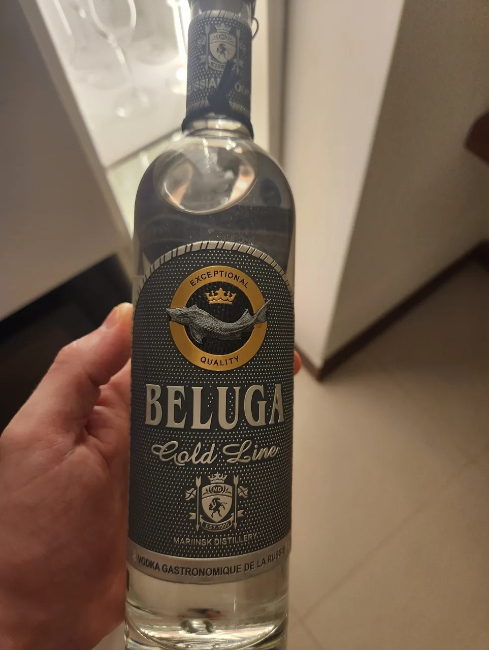 Mão segurando uma garrafa de Beluga Vodka Gold Line, com o esturjão gravado no rótulo