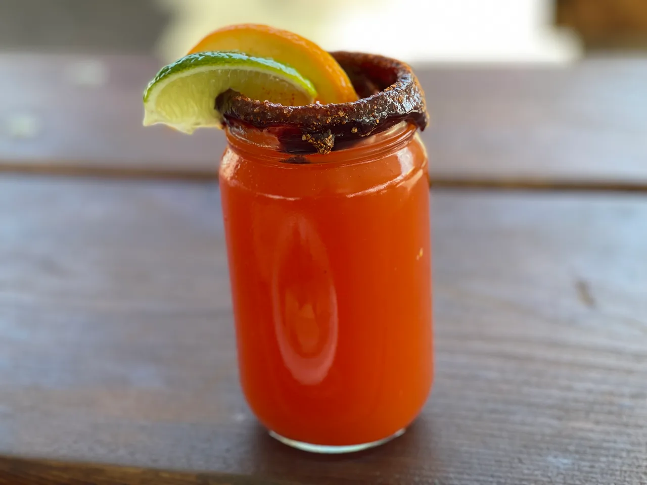 Michelada vermelha em copo alto com borda de sal e pimenta, fatias de limão e laranja