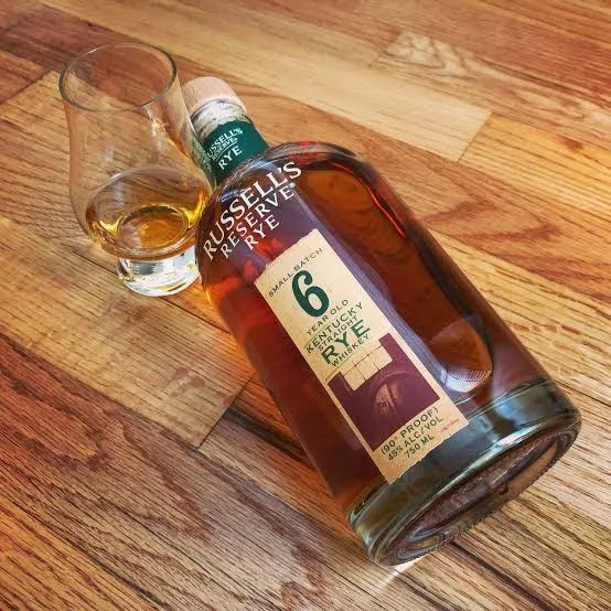 Garrafa de Russell's Reserve Rye de 6 anos deitada ao lado de uma taça de degustação