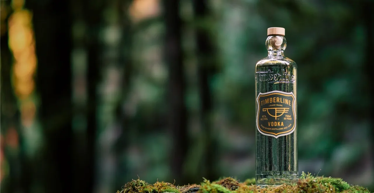 Garrafa de Timberline Vodka sobre musgo, com floresta de coníferas desfocada ao fundo